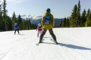 Adult skiing with two children on a snowy mountain slope